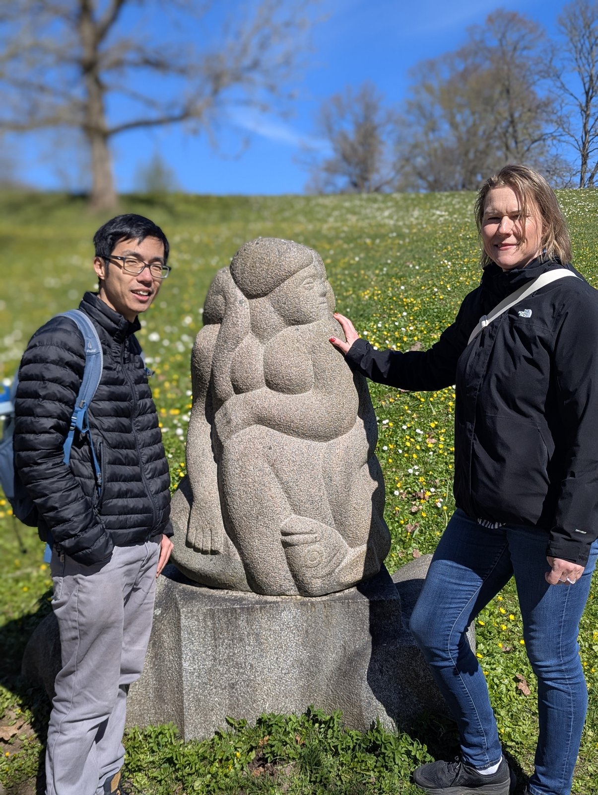 Daiga and a guest beside the seated mother-and-child sculpture at the Hill of Dainas, Turaida