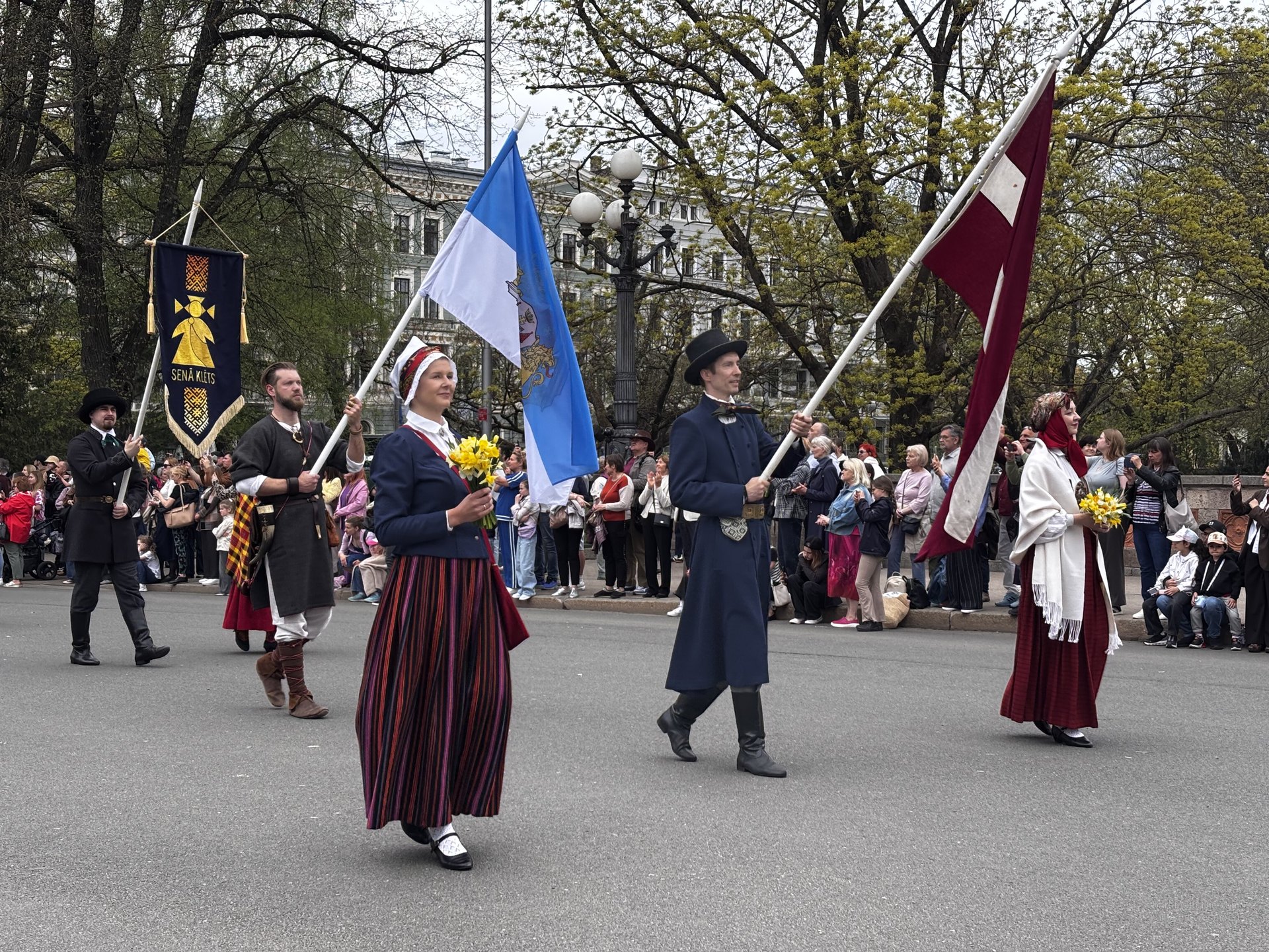 People in Latvian folk dress carrying flags during Independence Day celebrations in Riga